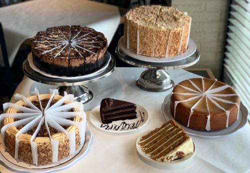A display of various cakes on stands, including chocolate, carrot, and layered cakes, arranged on a table.