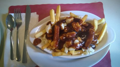 A plate of poutine featuring fries topped with cheese curds and gravy, served with cutlery on the side.