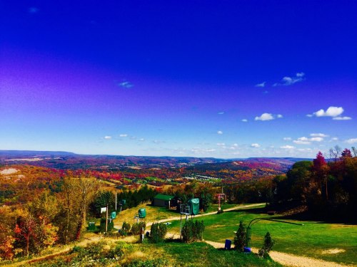 A scenic view of rolling hills and colorful autumn foliage under a bright blue sky with fluffy clouds.