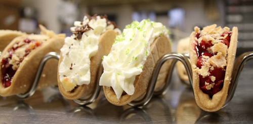 A row of dessert tacos filled with various toppings like whipped cream, fruit, and chocolate.