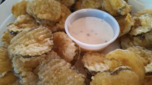 A plate of crispy fried pickles served with a small cup of ranch dressing.