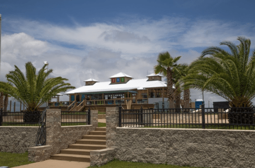 A beachside building with a white roof, surrounded by palm trees and a stone pathway under a blue sky.