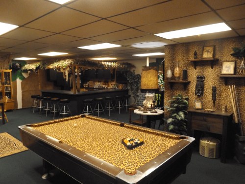 A themed game room featuring a leopard print pool table, bar area, and tropical decor.