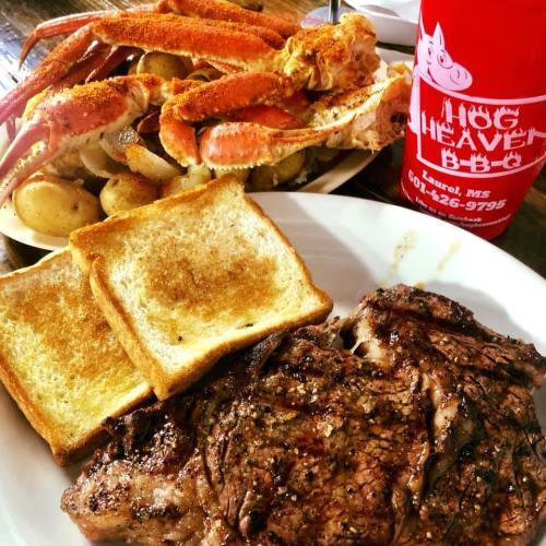 A plate of grilled steak, crab legs, seasoned potatoes, and two slices of toasted bread, alongside a drink.