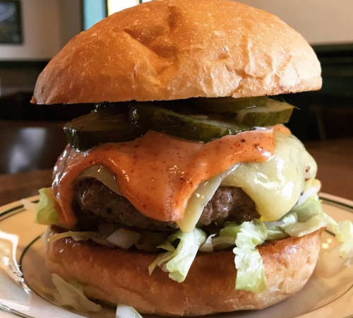 A juicy burger with lettuce, pickles, melted cheese, and a creamy sauce, served in a toasted bun.