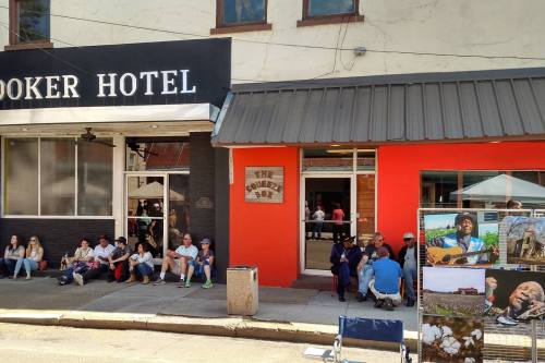 A street scene featuring the Cook Hotel, people sitting outside, and a display of photos and a musician with a guitar.