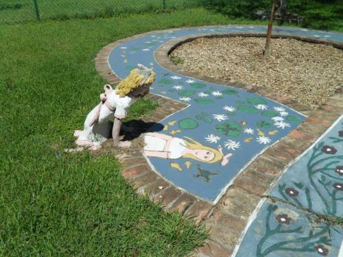 A whimsical garden scene featuring a painted pathway and a statue of a girl with a straw hat near flower designs.