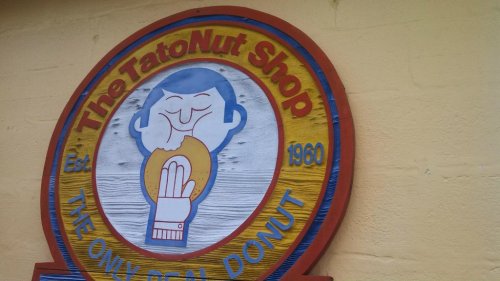 Sign for The TatoNut Shop, featuring a smiling character holding a donut, established in 1960.