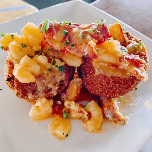 Two golden-brown fritters topped with creamy lobster and macaroni, garnished with chopped chives on a white plate.