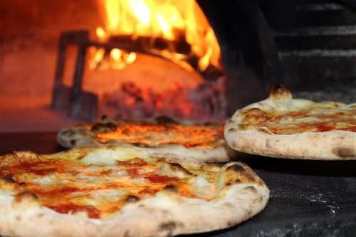Three pizzas baking in a wood-fired oven, with flames and glowing embers in the background.