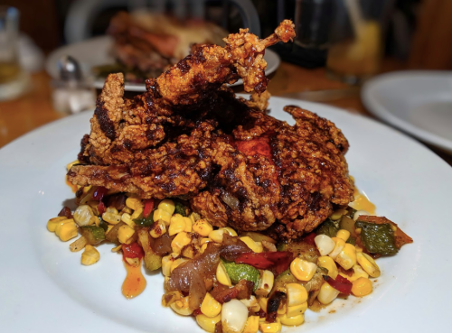 A plate of crispy fried chicken atop a colorful mix of corn and sautéed vegetables.