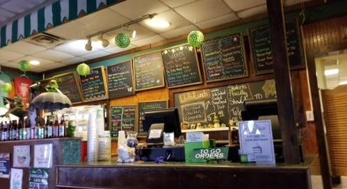 A cozy restaurant counter with a chalkboard menu, colorful decorations, and a display of drinks.