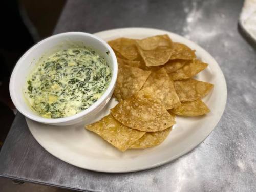 A plate of crispy tortilla chips served with a bowl of creamy spinach dip.
