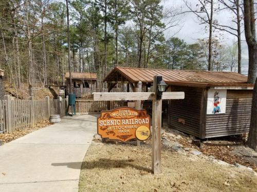 Pathway leading to a wooden sign for the Pine Mountain Scenic Railroad at Stockmar Park, surrounded by trees.