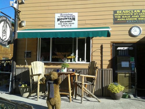 A cozy mountain recovery shop with outdoor seating, a sign for breakfast and espresso, and a bear statue in front.