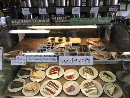 Display case filled with various desserts, including cakes and pastries, with labels for dietary options like vegan and gluten-free.
