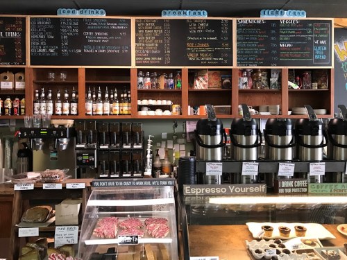 A cozy café counter displaying a menu, coffee machines, and baked goods in a warm, inviting atmosphere.