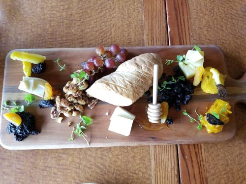 A wooden platter featuring assorted cheeses, grapes, honey, nuts, and dried fruits arranged artfully.