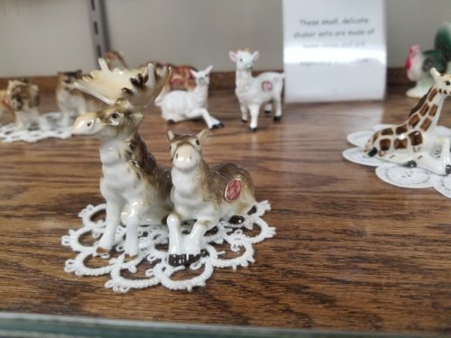 A porcelain moose and calf figurine on a lace doily, surrounded by other small animal figurines on a wooden shelf.
