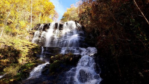 A cascading waterfall surrounded by vibrant autumn foliage and a clear blue sky.