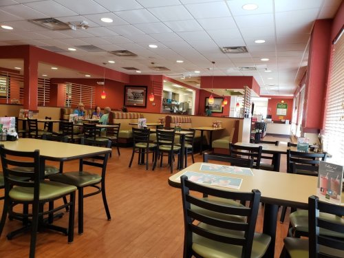 Interior of a casual dining restaurant with empty tables, booths, and patrons in the background. Bright and inviting atmosphere.