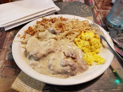 A plate of breakfast featuring scrambled eggs, hash browns, and biscuits smothered in creamy sausage gravy.