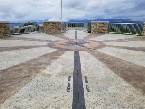 A compass rose design on a stone platform with a scenic view of mountains and cloudy skies in the background.