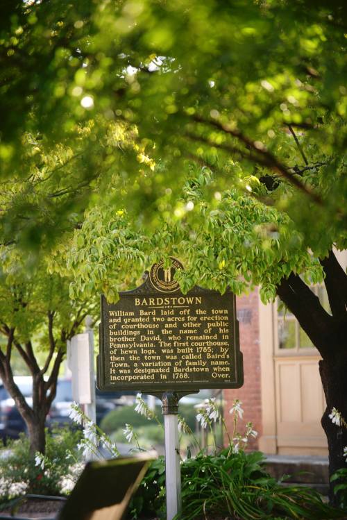 A historical marker in Bardstown, surrounded by green trees, detailing the town's founding and history.