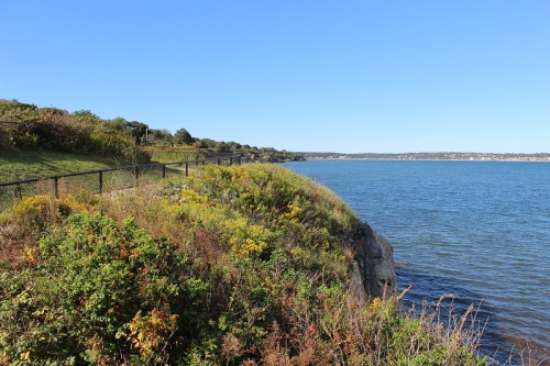A scenic view of a grassy cliff overlooking a calm blue lake under a clear blue sky.