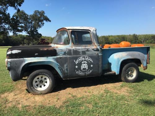 An old blue pickup truck with a rustic finish, parked in a field, loaded with pumpkins.