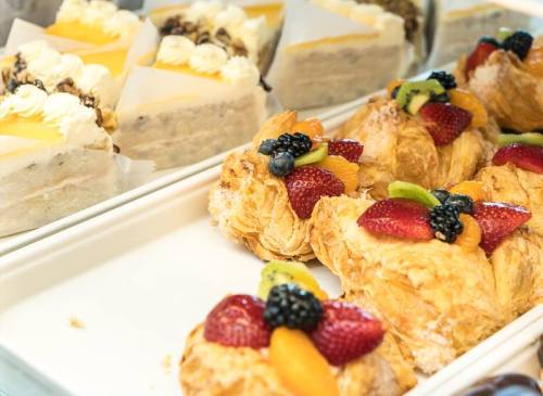 A display of pastries, including fruit-topped croissants and layered cakes with cream and fruit.