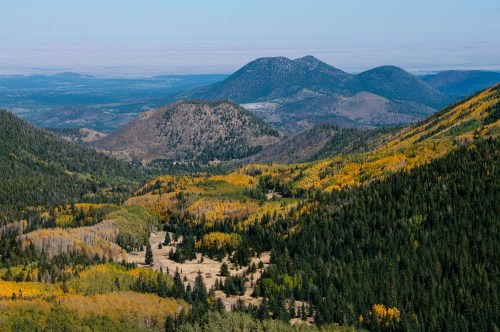 A scenic view of mountains and valleys, featuring vibrant autumn foliage and a clear blue sky.