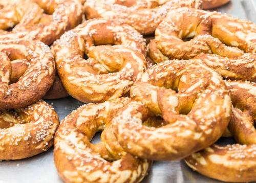 A close-up of freshly baked pretzels sprinkled with coarse salt, arranged in a pile on a tray.