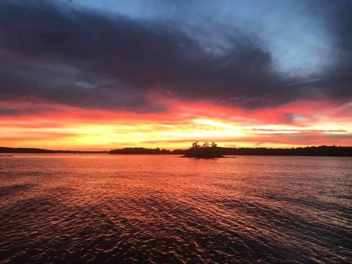 A vibrant sunset over a calm lake, with colorful clouds reflecting on the water and a small island in the distance.