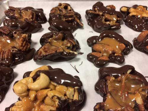 A tray of chocolate clusters with nuts and caramel, featuring almonds, pecans, and cashews on parchment paper.