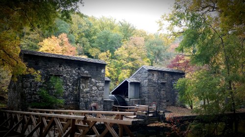 Historic stone structures surrounded by vibrant autumn foliage and a wooden bridge in a serene natural setting.