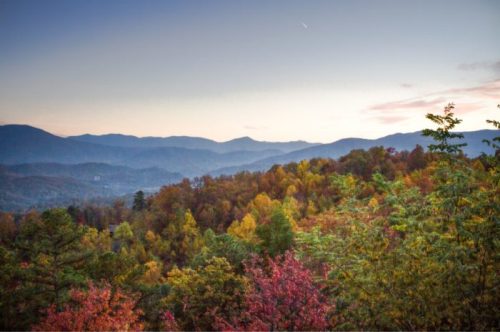 A scenic view of mountains and colorful autumn foliage under a clear sky at dusk.