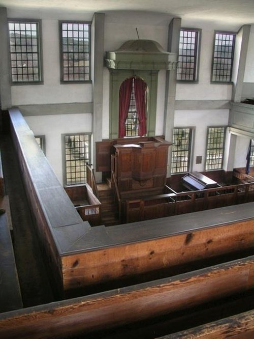Interior view of a historic church, featuring wooden pews, a pulpit, and large windows with natural light.