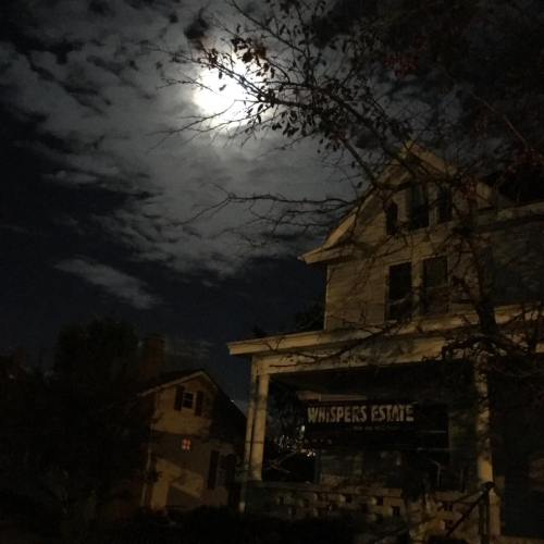 A spooky house under a full moon, with dark clouds and bare trees, creating an eerie nighttime atmosphere.