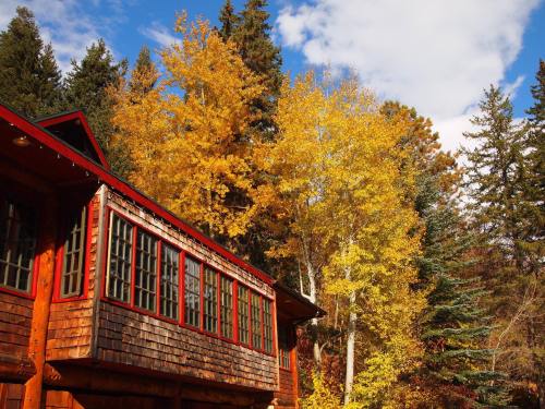 A rustic wooden cabin surrounded by vibrant autumn trees with yellow and green leaves under a blue sky.