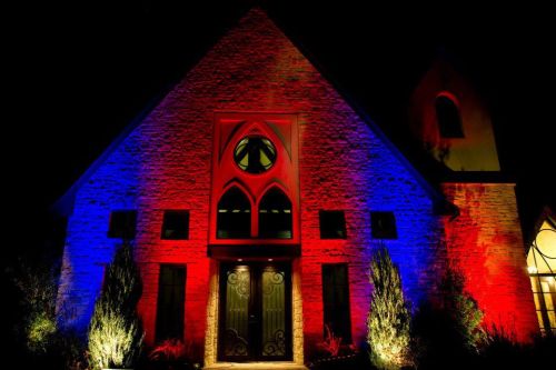 A stone building illuminated with red and blue lights at night, featuring arched windows and a tall spire.