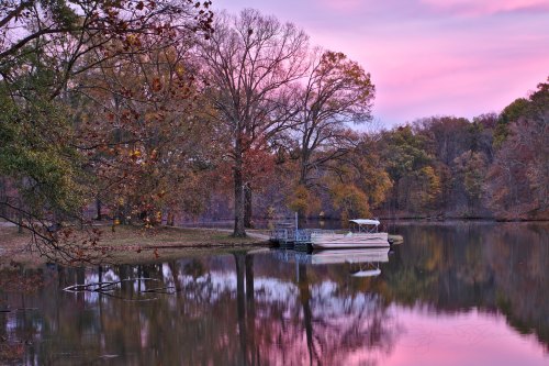 A serene lake at sunset, with a dock and colorful autumn trees reflecting in the water.