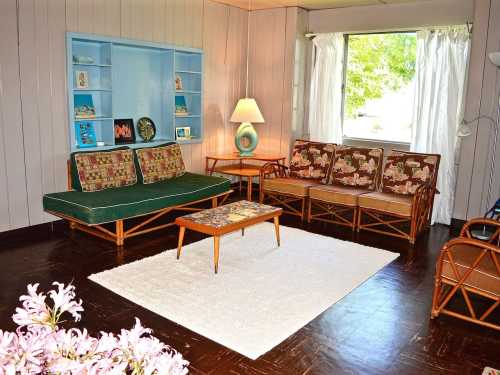A cozy living room with rattan furniture, a coffee table, and a large window letting in natural light.
