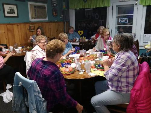 A group of women gathered around a table, enjoying crafts and conversation in a cozy, colorful setting.