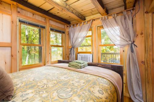 Cozy bedroom with wooden walls, large windows, and a neatly made bed with a decorative blanket and towels.