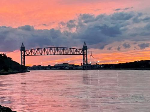 A bridge spans a calm river at sunset, with vibrant pink and orange skies reflecting on the water.
