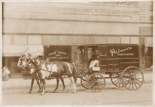 A vintage horse-drawn delivery wagon for Palmer's Pure Candies parked on a city street.