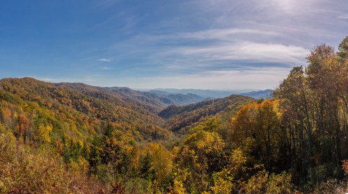 A panoramic view of colorful autumn mountains under a clear blue sky, showcasing vibrant foliage and rolling hills.