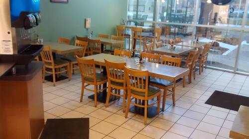 A spacious restaurant interior with empty tables and chairs, featuring a drink station in the corner.