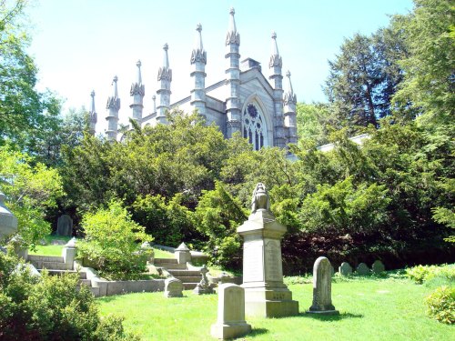 A historic mausoleum surrounded by lush greenery and gravestones in a serene cemetery setting.